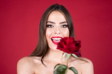 Gül çiçekli gülümseyen bir kadının portresi. Güzel manken kadın yüzü. Yüzünde kırmızı bir gül olan güzel bir genç kızın portresi. Vogue bahar yaz tarzı. Değiştirilmemiş yüz yok