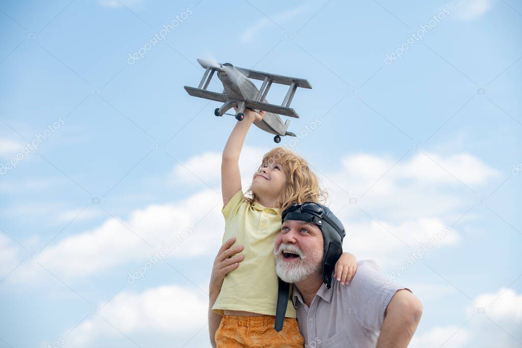 Grandfather and grandson enjoying play with plane together on blue sky. Cute child with granddad playing outdoor