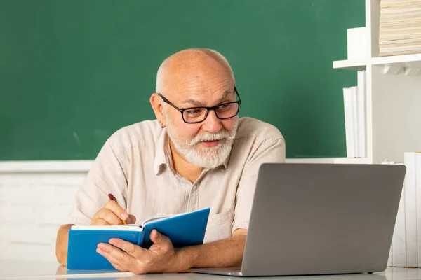 Portrait of senior teacher teaching line of high school students with notebook in classroom on blackboard. Grandfather education concept