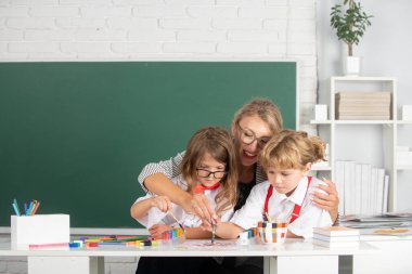 Schoolkids with teacher. Happy children from elementary school study at draw lesson. Pupils girl and boy with teacher painting at art school. School education and children concept