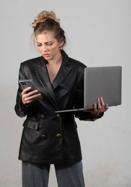 Dizüstü bilgisayar kullanan ciddi bir kadın. Bilgisayarı ve telefonu olan siyah elbiseli bir iş kadını.