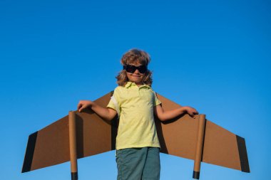 Çocuk yaz parkında oyuncak uçak kanatlarıyla oynuyor. Yenilik teknolojisi ve başarı konsepti. Mavi gökyüzüne karşı çocuk pilot. Çocuk pilot parkta çimlerde eğleniyor.