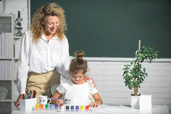 Schoolgirl drawing with teacher. Children from elementary school study at draw lesson. Pupil girl with mother teacher painting. School education and children concept