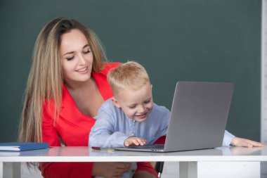 Dizüstü bilgisayar kullanan okul çocuğu. İlkokul öğretmeni ve öğrenci sınıfta. Anne ve oğlu birlikte bilgisayar laptopu kullanıyorlar.