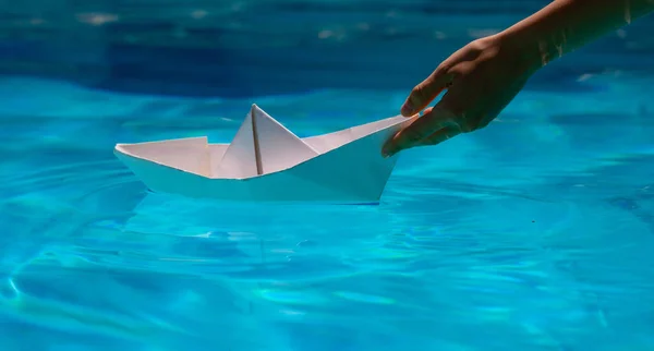 Paper boat with hand. Paper boat sailing on blue water surface. Origami paper boat