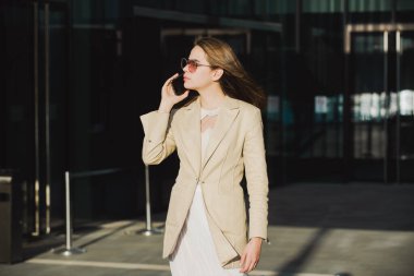 Havalı yaz bahar kıyafetleri içinde dışarıda telefonda konuşan güzel bir iş kadını. Kadın stili model şehir caddesinde yürüyor. Yaz trendi, moda kıyafeti