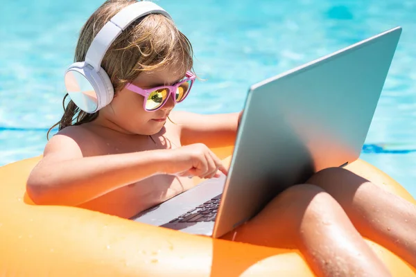 Child working on laptop in summer pool. Little freelancer using computer, remote working in poolside
