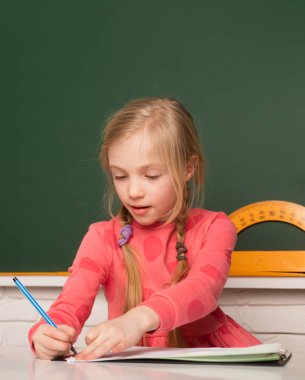 School concept. Kids drawing in notepad. Little girl pupil study in classroom. School student taking notes from book for study