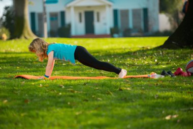 Child is pushing up on the green grass. Boy doing push-ups in the yard. Kid pushing up