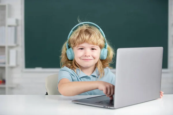 Happy boy in headphones watch video lesson on computer in school, child in earphones have online lesson, using laptop