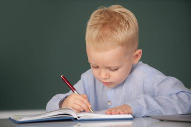 Little schoolboy study in a classroom at elementary school. Kid writing in notebook in class. Education and kids knowledge concept