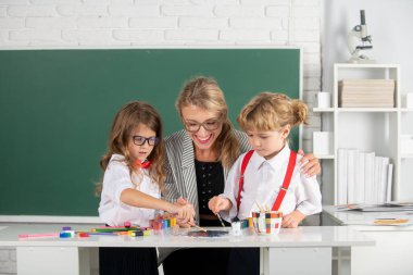 Schoolkids drawing with teacher. Children from elementary school study at draw lesson. Pupils girl and boy with teacher painting at art school. Education and knowledge