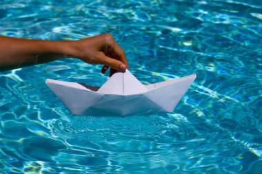 Paper boat sailing on water causing waves and ripples. Tourism and traveling, travel dreams vacation holiday, sailing adventure. Hand putting a paper boat into water