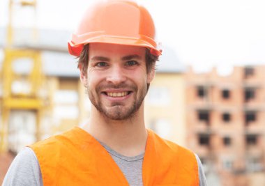 Construction worker man in work clothes and a construction helmet. Portrait of positive male builder in hardhat working at construction site