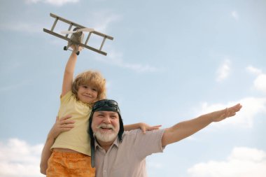 Grandfather and grandson having fun with plane outdoor on sky background with copy space. Child dreams of flying, happy childhood with granddad