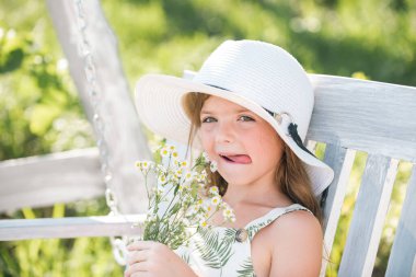 Spring kids portrait, funny face. Beautiful blond little child girl with long hair smelling flower. Spring child face. Funny kids face. Happy little blond hair child with flowers