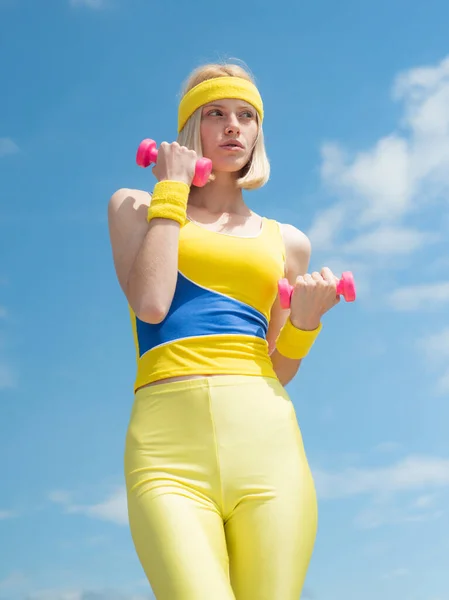 Blonde girl doing sport exercises with dumbbells at sky background. Leisure time sport activities. Beautiful girl take care about her health drinking water and doing sport exercises