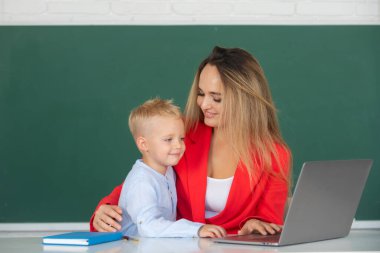 Little school child son using laptop with mother. Elementary school classroom. Teacher and schoolchild pupil in class. Mother and son together using computer laptop