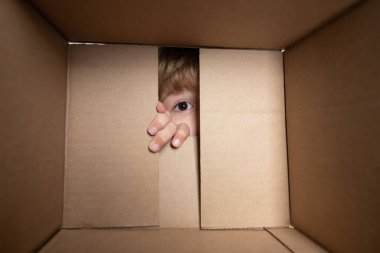 Amazed adorable little boy peeking inside gift box, unpacking present with funny astonished expression, impatient child unboxing surprise. Close up eyes looking