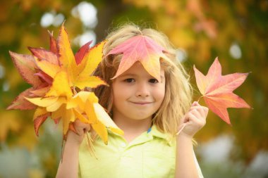 Kids play in autumn park. Children throwing yellow leaves. Child boy with oak and maple leaf outdoor. Fall foliage. Toddler or preschooler in fall autumn nature