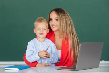 Öğretmen okulda okul çocuğuna yardım ediyor. Anne ve oğlu birlikte bilgisayar laptopu kullanıyorlar. Okul çocuğu çevrimiçi eğitim öğreniyor