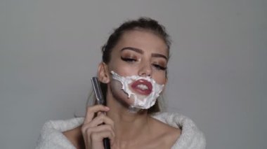 Kadın traş suratı. Güzel beyaz bir kadın yüzünü jiletle tıraş ediyor. Yüzünde tıraş köpüğü olan güzel bir kız.