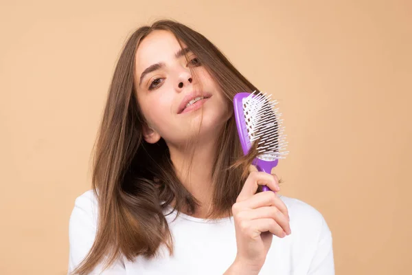 Smiling woman brushing hair with comb. Beautiful girl combing long hair with hairbrush