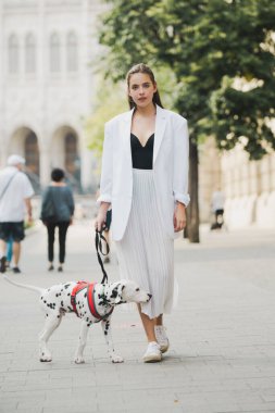 Sokakta yürüyen zarif genç bir kadının açık hava portresi. Genç manken köpekle yürüyor, şehir tarzı.