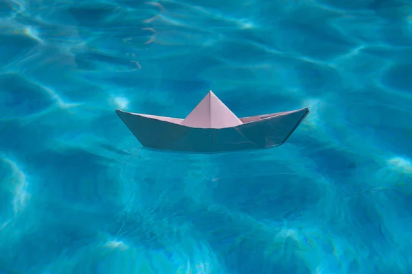 Paper boat sailing on water causing waves and ripples. Paper boat into water. Concept of tourism, travel dreams vacation holiday. Blue water background