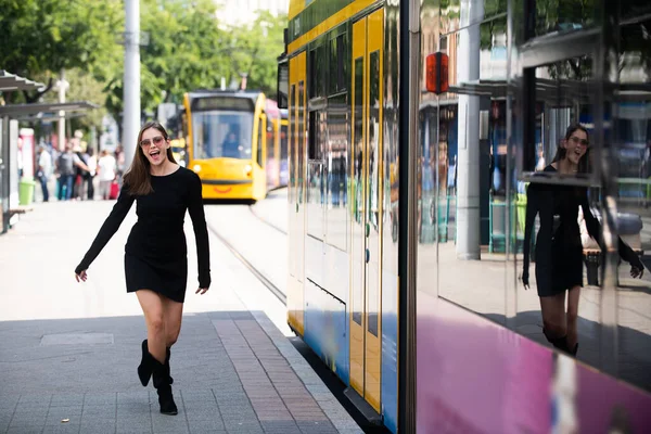 Fashionable woman running after bus trolleybus and pulling trolley case on the street, fashion street style