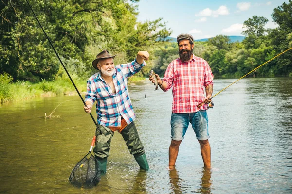 Man friends. Two men friends fishing. Flyfishing angler makes cast, standing in river water. Old and young fisherman