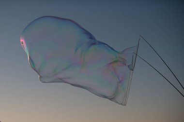 Mavi bulutlu gökyüzüne karşı havada büyük sabun baloncukları patlatıyorlar. Gökyüzünde yüzen büyük baloncuk, gökyüzü parlak mavi arkasında, kabarcık şeffaf ama spektrumun renklerini yansıtıyor