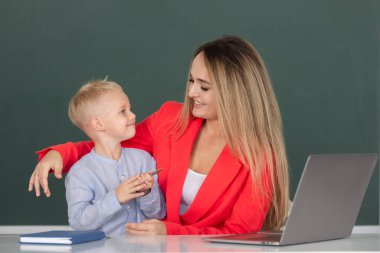 Anne ve oğlu birlikte bilgisayar laptopu kullanıyorlar. Okul çocuğu çevrimiçi eğitim öğreniyor. Öğretmen çocukların ders almasına yardım ediyor.