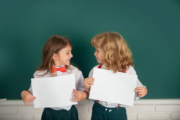 白い紙を持っている2人の学生 コピースペースのあるポスター 小学校の教室で勉強している2人の幸せな子供の肖像画 子供教育のための空白のメモ用紙 — ストック写真