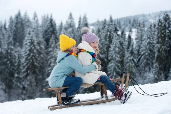 そりに乗っている子供たち 子供の男の子と女の子は雪の中で外で遊ぶ クリスマス — ストック写真
