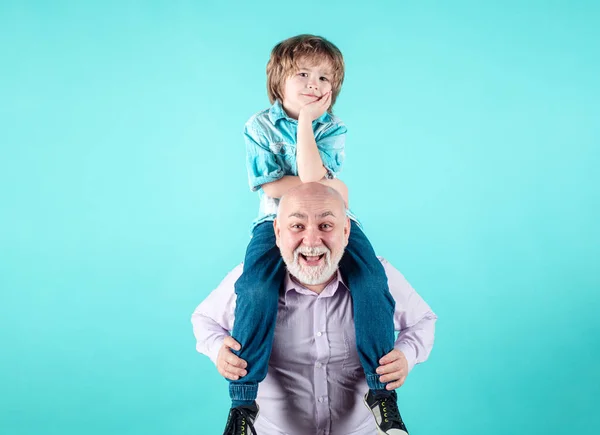 Grandson child and grandfather piggyback with funny face isolated on blue in studio. Granddad and cute boy with funny face. Elderly old relative with child
