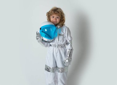 Uzay giysisi içinde, gri arka planda izole edilmiş miğfer tutan sevimli, küçük bir uzaylı çocuk. Başarı, yaratıcılık ve başlangıç konsepti