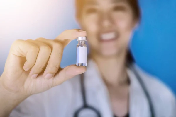一位迷人的医生 身穿一件白色外套 肩上戴着听诊器 手里拿着一瓶空白白标签的疫苗瓶 面带微笑 保健和医疗概念 图库照片