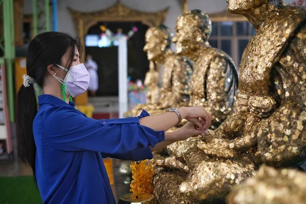 アジアの女性がタイの寺院で仏像に細い金箔を金箔で金箔をつけている 仏像の腕に金箔を貼ったり貼ったりする — ストック写真