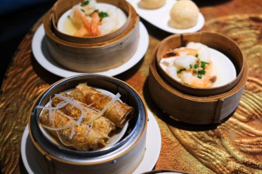 Çin restoranındaki ahşap bir masada yuvarlak bambu vapurlarda servis edilen çeşitli kızarmış ve buğulanmış Çin hamur köftesi tabakları..