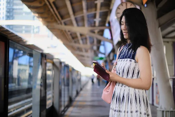 Çekici, kendine güvenen Asyalı bir iş kadını sabah işe gitmek için istasyonda trenini beklerken cep telefonunu kullanıyor..