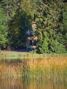 Finlandiya 'nın Hameenlinna kentindeki Aulanko doğa koruma ve dinlenme alanında Neogotik stil Ruusulaakso pavyonu ve Metsalampi: sonbahar, renkli ağaçlar, yansıma.