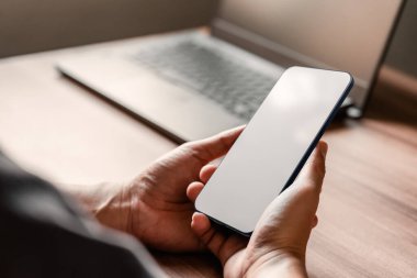 Mockup image of a man holding and using smartphone with blank desktop screen while working and drinking coffee in cafe.
