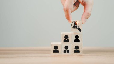 Büyüteçle el ele tutuşan tahta küpleri, işe alım müdürleri için ekip lideri olacak en iyi çalışan ikonuna ve müşteri kavramlarına odaklanır. HRM veya İnsan Kaynakları Yönetimi.