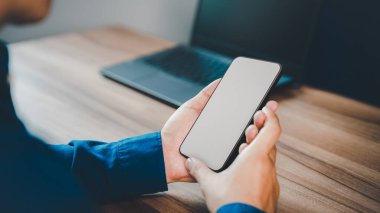 Mockup image of a man holding and using smartphone with blank desktop screen while working and drinking coffee in cafe.