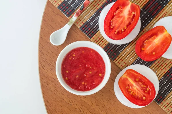 Fresh tomato puree in a small white bowl and cotton pads. Homemade face or eye mask, natural beauty treatment and spa recipe. Top view, copy space.