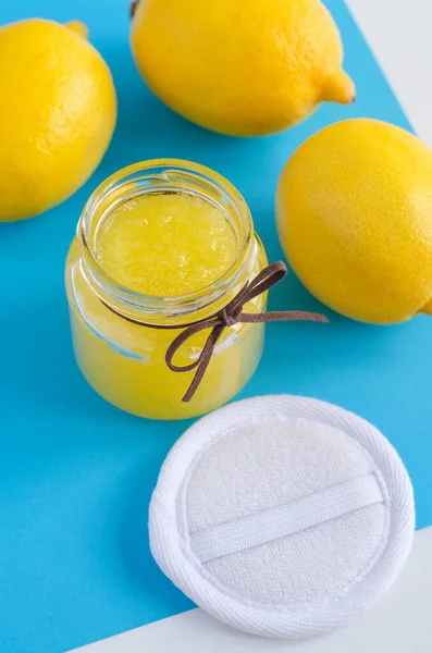 Homemade lemon facial mask (exfoliating sugar scrub, foot soak) in a small glass jar and face sponge. DIY citrus beauty treatment and spa recipe.