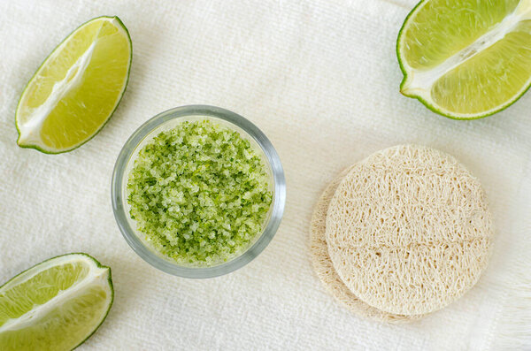 Домашний фруктовый скраб из лайма (соль для ванн, мазь для ног, маска для лица или волос) в маленькой стеклянной миске и мочалках. Лечение природной красоты, уход за волосами и спа рецепт. Вид сверху, пространство для копирования. 