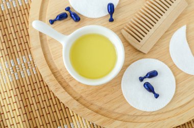 Küçük beyaz kase kozmetik (masaj, temizlik) yağı, yüz serumu kapsülleri ve pamuk göz bantları. Doğal cilt bakımı, spa ve güzellik tedavi tarifi. Üst görünüm, alanı kopyala. 