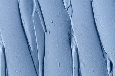 Açık mavi bentonit yüz kilini (aljinat maskesi, yüz kremi, vücut sargısı) kapat, seçici odaklanma. Fırça darbeleriyle soyut arkaplan. 